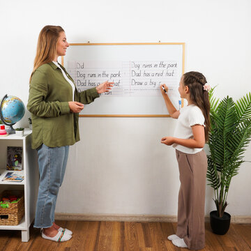 A focused educator provides individual guidance to a young girl, helping her master grammar rules and sentence structure using a set of colorful magnetic alphabet cards.