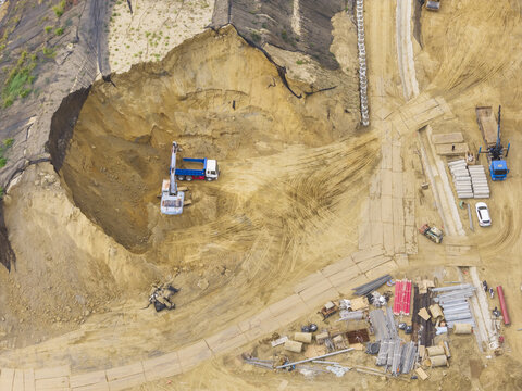 Aerial view of an excavation site with heavy machinery, trucks, and construction materials on sandy ground in Taiwan.