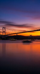 Fototapeta premium Breathtaking sunset paints a grand suspension bridge and silhouetted cityscape with vibrant hues