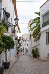 Spain, Altea city. Narrow cobblestone street lined with whitewashed buildings, potted plants, and traditional lanterns in a picturesque Mediterranean village © JuLady_studio