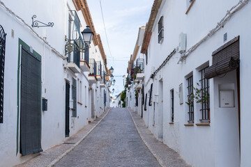 Spain, Altea city. Narrow cobblestone street lined with whitewashed buildings and balconies in a picturesque Mediterranean village setting © JuLady_studio