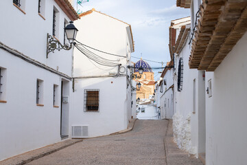 Spain, Altea city. Narrow cobblestone street lined with whitewashed buildings and traditional architecture in a quaint village setting under a clear sky © JuLady_studio