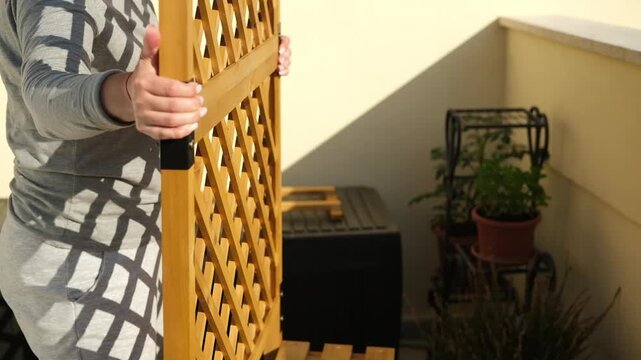 Person Assembling Wooden Plant Stand With Trellis on Balcony During Urban Gardening Project
