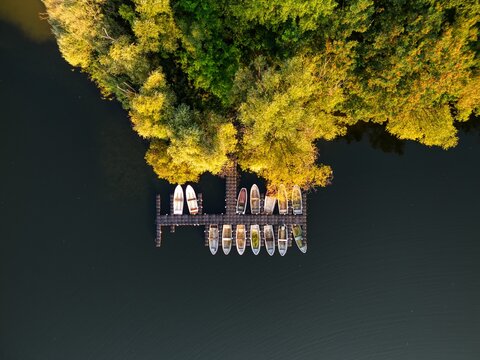 Aerial view of Lake Tegel with small rowing boats moored at a wooden pier along a lush forest shoreline during golden hour in Berlin, Berlin, Germany.