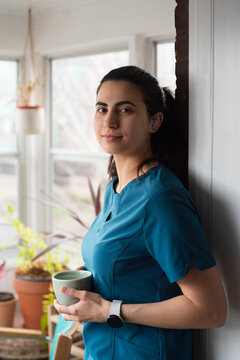 Nurse Stands by Window Holding Cup During Break in a Bright Room
