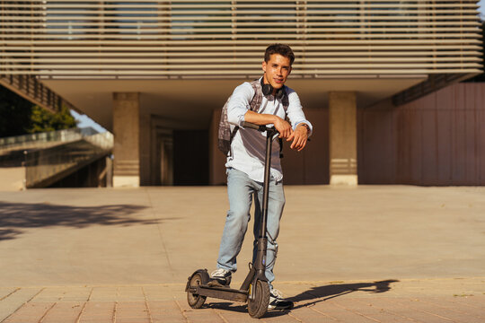 Confident teenage guy wearing shirt standing on scooter