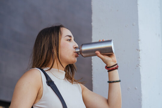 Thirsty young female student drinking from flask