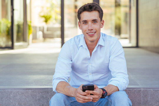 Cheerful young male in stylish outfit sitting on porch
