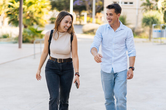 Cheerful college friends chatting and walking on pavement