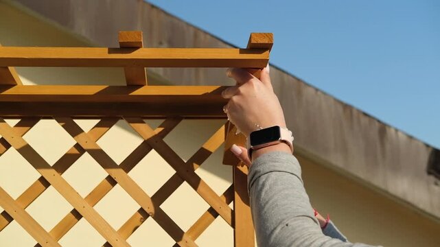 Person Assembling Wooden Plant Stand With Trellis on Balcony During Urban Gardening Project