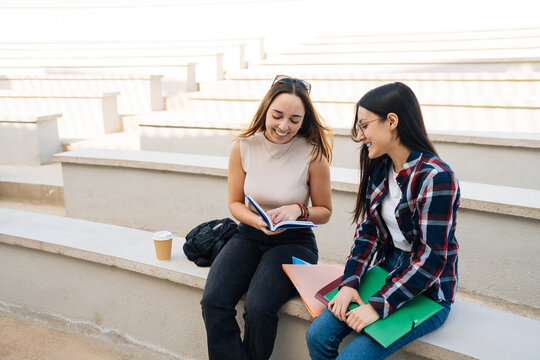 Cheerful classmates sitting on stairs while studying textbook