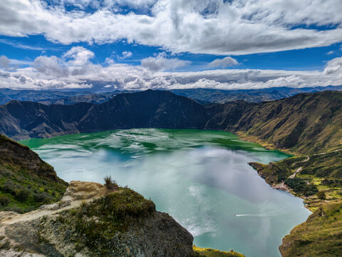 Aerial view of Quilotoa Lake with its emerald green water surrounded by steep volcanic crater walls under a dramatic cloudy sky Cotopaxi, Ecuador.