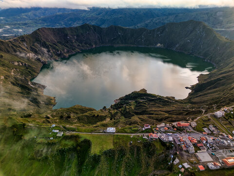 Aerial view of Quilotoa Lake with its emerald green water inside a volcanic crater surrounded by steep ridges and a small village in Cotopaxi, Ecuador.