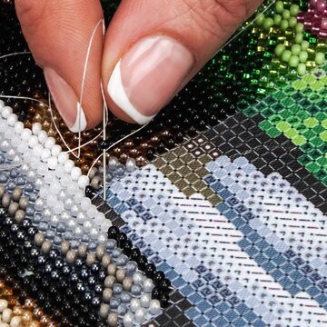 Detailed shot of a woman's hand carefully sewing bright beads onto canvas. Concept of handmade jewelry, traditional crafting, hobby, and creative leisure activity at home studio.