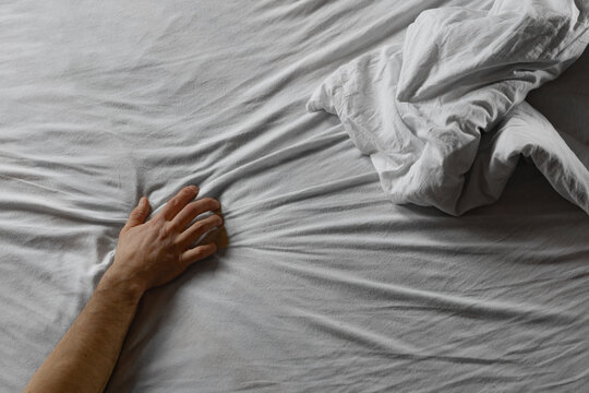 Person Reaches for Blanket on Bed in Morning Light