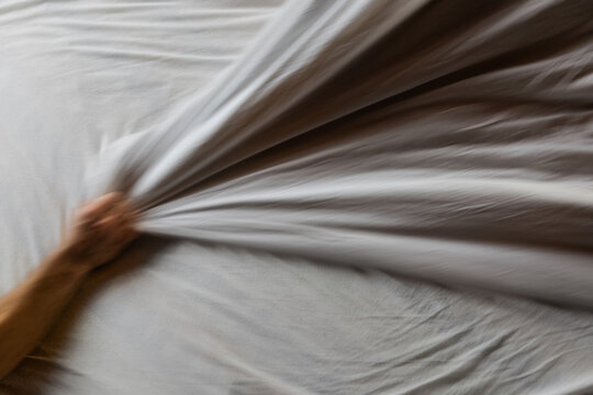 Making a Bed With Freshly Washed Sheets and a Hand Pulling the Fabric