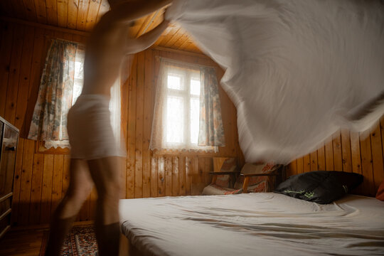 Person Making a Bed in a Wooden Room With Natural Light