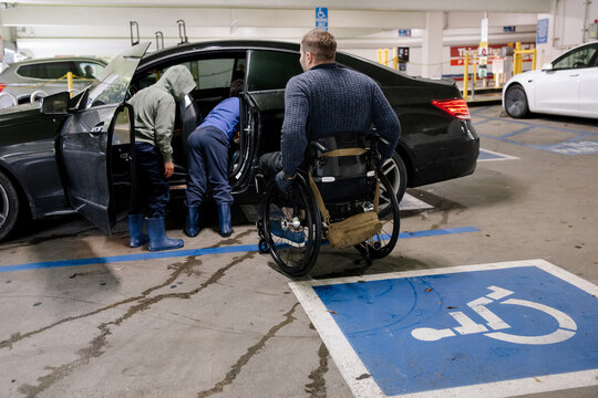 Person in Wheelchair and Assistants Near Accessible Car in Parking Lot