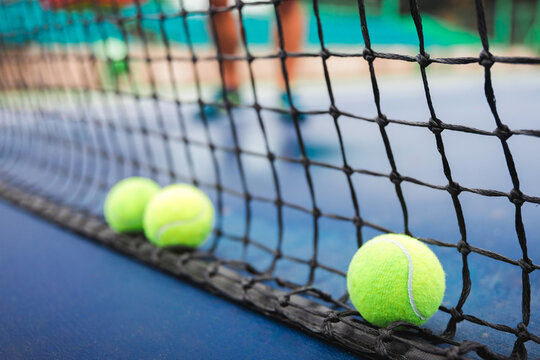 Tennis Balls Resting Against Net on Court Surface