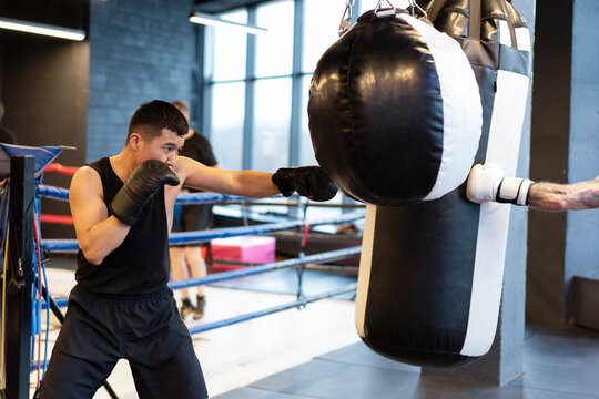 Male Asian Boxer Punching Heavy Bag with Extended Jab in Gym
