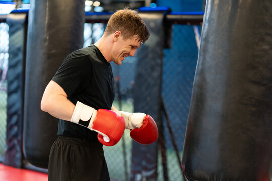 Male Boxer Smiling While Hitting Heavy Bag Between Row of Bags