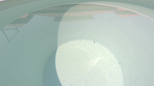 Close-up view of clear water inside a large ceramic container, gently rippling due to wind movement. The surface reflects natural sunlight, creating dynamic light patterns and subtle motion.