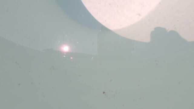 Close-up view of clear water inside a large ceramic container, gently rippling due to wind movement. The surface reflects natural sunlight, creating dynamic light patterns and subtle motion.