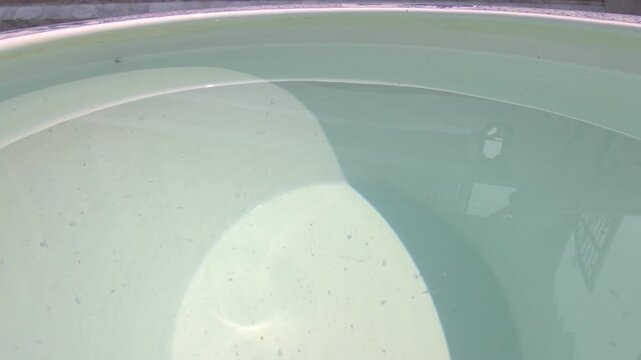 Close-up view of clear water inside a large ceramic container, gently rippling due to wind movement. The surface reflects natural sunlight, creating dynamic light patterns and subtle motion.
