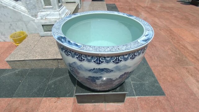 Close-up view of clear water inside a large ceramic container, gently rippling due to wind movement. The surface reflects natural sunlight, creating dynamic light patterns and subtle motion.
