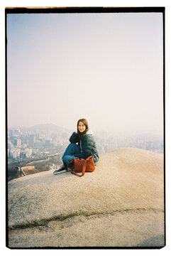 Young woman sitting on mountain top enjoying Seoul cityscape view