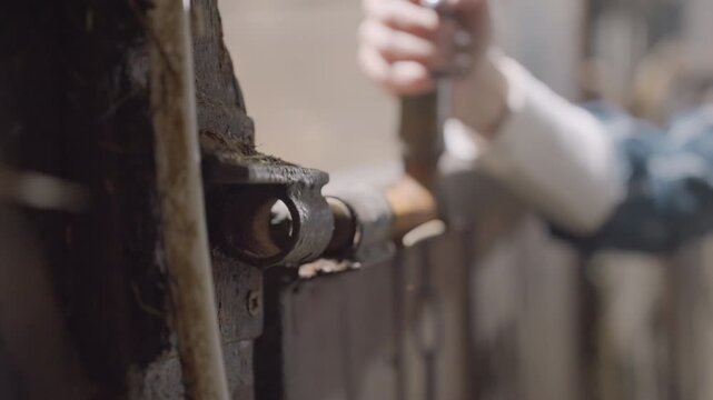 Closeup rusty metal hinge white hand cleaning corrosion with small brush in dim barn workshop, craftsman restoring vintage gate, tactile grime, oil droplets, weathered wood, focused technique