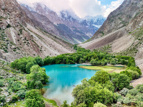 Aerial view of a turquoise lake surrounded by lush green trees in a deep mountain valley with Vudor Peak in the background Rushon, Gorno-Badakhshan, Tajikistan.
