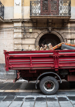 Red Truck Carrying Discarded Items Near Old Building