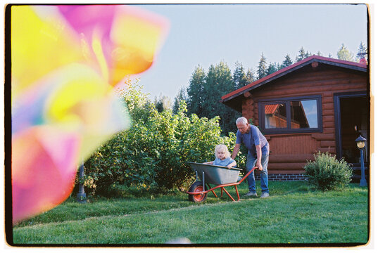 A great-grandfather gives his great-grandson a ride in a wheelbarrow