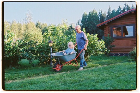 A great-grandfather gives his great-grandson a ride in a wheelbarrow