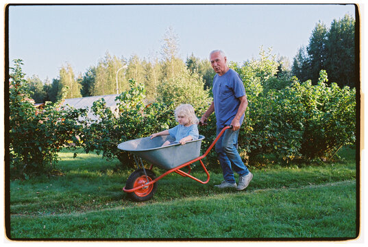 A great-grandfather gives his great-grandson a ride in a wheelbarrow