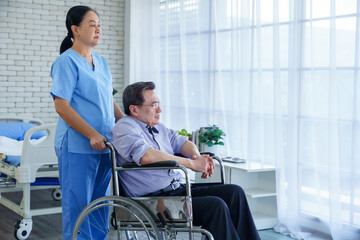 Obraz premium The nurse is pushing the asian a man in wheelchair Look out the window hospital room. copy space