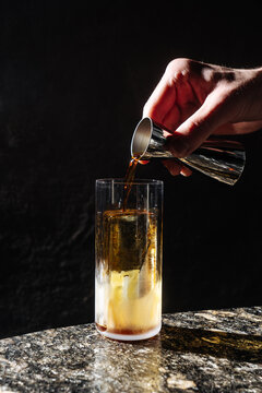 Hand Pouring Dark Liquid into Highball Glass with Ice