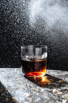 Dark cocktail with ice and mist on marble surface