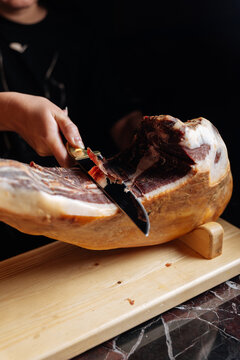 Hand slicing cured ham with knife on wooden stand