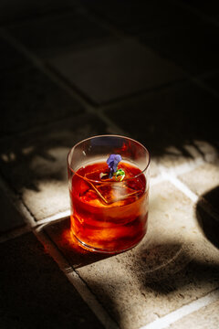 Amber cocktail with ice and flower garnish on sunlit tile floor