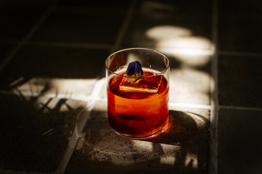 Negroni cocktail with ice cube and flower garnish on stone surface