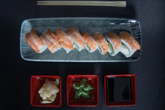 Cream Cheese and Avocado on a Grey Plate with Wasabi, Ginger and Soy Sauce, Japanese Cuisine on Black Background . Ebi Sushi Roll topped with Steamed Shrimp,