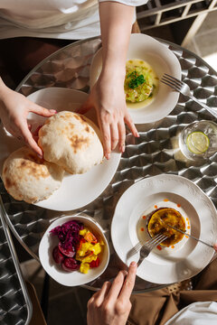 Hands sharing fresh flatbread with gourmet appetizers and pickled vege