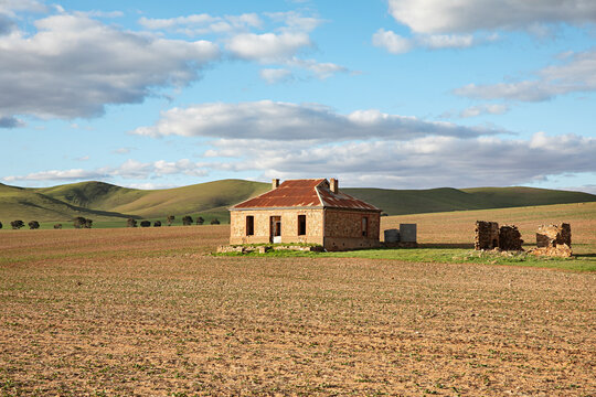 Abandoned stone cottage with rusty roof sits in a vast, dry field