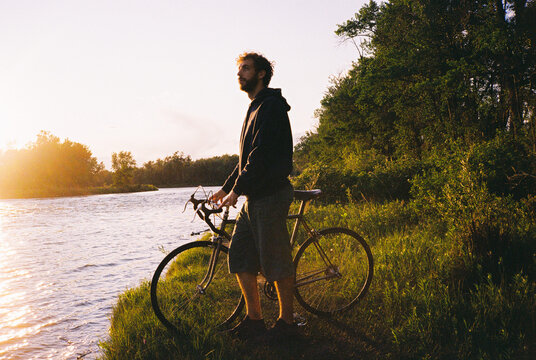 Man standing with the bicycle at the riverbank in summer 