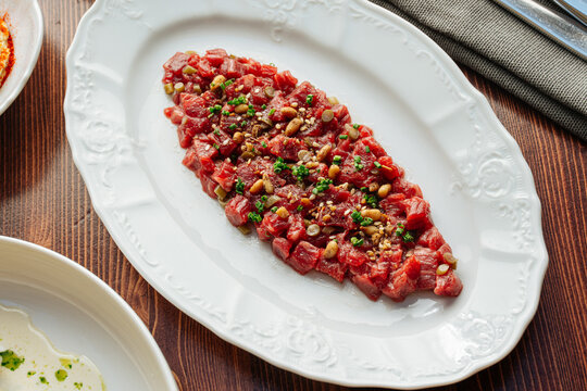 Beef tartare with herbs and pine nuts on white ceramic plate