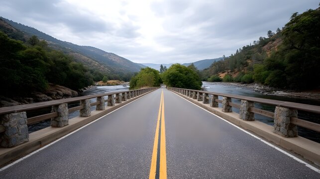 A straight roadway crosses over a flowing river connecting lush mountainous terrain under a dramatic overcast sky