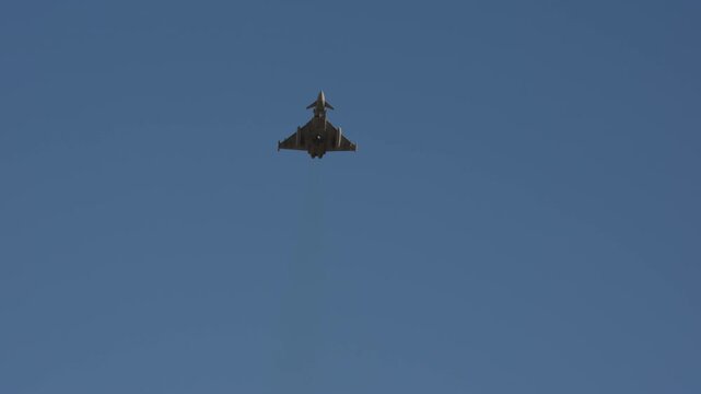 Delta canard wing military fighter jet seen from below in frontal view against clear blue sky filmed in slow motion