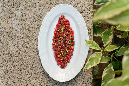 Beef tartare with herbs and pine nuts on white plate